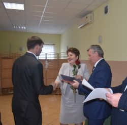 dwie, trzy osoby wręczają innej dyplom i kwiaty